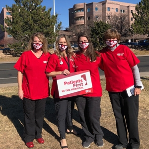Group of four nurses outside Longmont Hospital hold sign "Patients First"