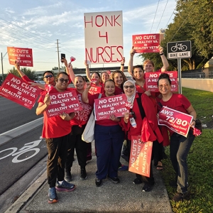 Group of nurses by side of the road smiling, holding signs "No Cuts: A Healthy VA = Healthy Vets"