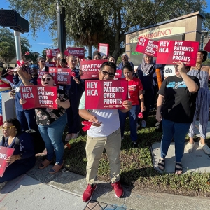 Large group of nurses outside hospital, holding signs "Hey HCA, Put Patients Over Profit"