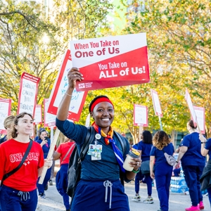 Nurse on picket line holding sign "When You Take On One Of Use, You Take On All Of Us"