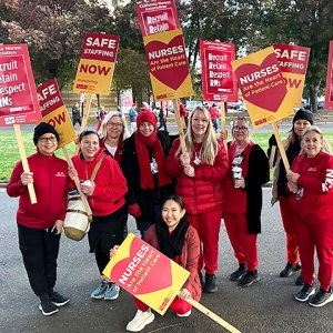 Group of nurses outside holding signs "Safe Staffing NOW", "Recruit, Retain, Respect RNs", and "Nurses are the heart of patient care"