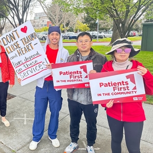 Nurses outside hold signs "Patients First in the Hospital", "Patients First in the Community", and "Don't Close Trauma and Heart"