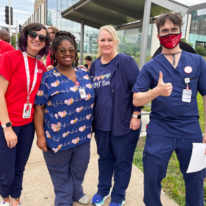 Four SLU Hospital nurses smiling in front of hospital, one giving a thumbs up.