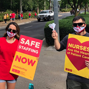 Two nurses holding signs "Safe staffing now" and "Nurses are the heart of patient care"