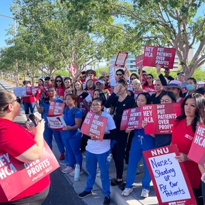 Large group of nurses outside hospital holding signs "Hey HCA Put Patients Over Profits" and more.