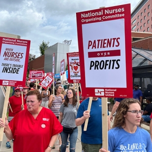 Nurses picketing outside hospital holding signs "Patients over Profits"