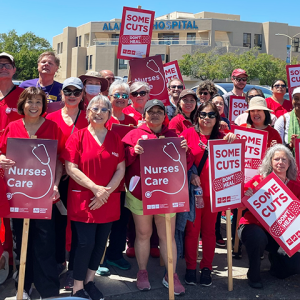 Alameda RNs in front of hospital holding signs "Some cuts don't heal" and "Nurses care"