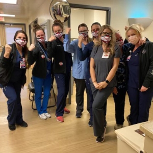 Group of nurses inside hospital, side-by-side, some with raisded arms/fists