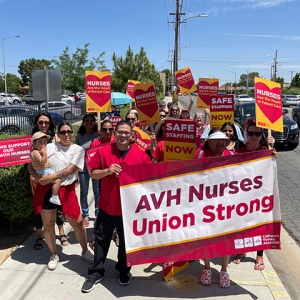 Group of nurses walking outside holding banner "AVH Nurses Union Strong" and signs "Nurses are the heart of patient care"