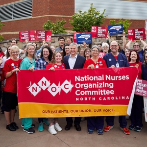 Large group of nurses standing with Josh Stein outside Mission Hospital holding an NNOC banner. Some hold signs "Josh Stein for Governor"