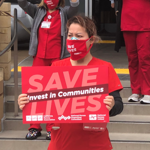 Nurse holds sign "Invest in Communities"