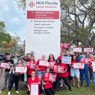 Large group of nurses outside HCA Florida Largo Hospital holding signs "Hey HCA Put Patients Over Profits" and more.