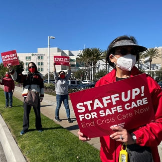 Four nurses standing outside hospital holding signs "Staff Up for Safe Patient Care"