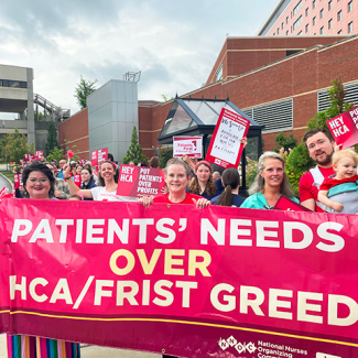 RNs at Mission Asheville holding signs and banner "Patients' needs over HCA/FRIST greed" and "Hey HCA, put patients over profits"