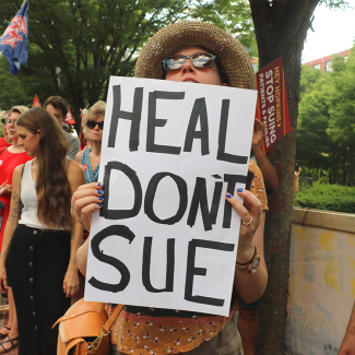 Woman holds sign "Heal Don't Sue"